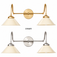 A cream two-light gooseneck wall sconce with glossy cone shades, shown in Cream with brass or nickel hardware. It has two curved gooseneck arms joined by a straight crossbar at a round backplate, so it sits wide like a vanity light. Hang it over a bathroom mirror, above a kitchen sink, or over a farmhouse window. Warm off white pairs well with unlacquered brass, butcher block, and checkered tile, so it suits English cottage, vintage kitchen, and warm neutral rooms.