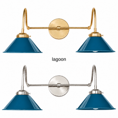 A deep peacock blue two-light gooseneck wall sconce with glossy cone shades, shown in Lagoon with brass or nickel hardware. It has two curved gooseneck arms joined by a straight crossbar at a round backplate, so it sits wide like a vanity light. Hang it over a bathroom mirror, above a kitchen sink, or over a home bar. Deep blue sits well with rust or ochre accents, velvet, and dark wood, so it suits moody traditional, jewel tone, and art deco rooms.