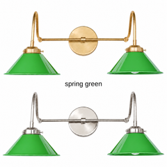 A kelly green two-light gooseneck wall sconce with glossy cone shades, shown in Spring Green with brass or nickel hardware. It has two curved gooseneck arms joined by a straight crossbar at a round backplate, so it sits wide like a vanity light. Hang it over a bathroom mirror, above a kitchen sink, or over a home bar. Bright green pairs well with pink walls, striped wallpaper, and rattan, so it suits preppy, Palm Beach, and colorful traditional rooms.