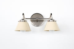 Two-light Double Kelly wall sconce in polished nickel with cream cone shades, clean modern bathroom vanity light with mid century inspired shape, ideal for double sink bathrooms, kids bath lighting, powder room sconces, and bedroom wall lamps, photographed on white background