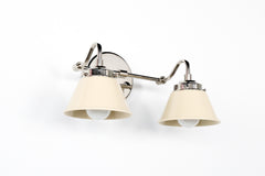 Angled view of the Double Kelly wall sconce in polished nickel with cream cone shades, modern mid century inspired two-light bathroom vanity fixture that works as a playful bedroom sconce or hallway wall light, sleek curved arms with soft neutral shades, shown on a bright white studio background