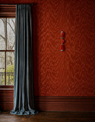 Flame Janus sconce with brass accents mounted on a poppy red moire wallpaper wall, styled beside icy blue pinch pleat velvet curtains, dark wood floors, and deep red painted trim. The geometric two-light sconce adds a playful, sculptural pop to a richly layered maximalist room, mixing colorful wall lighting with moody old-house character. Perfect for dopamine decor, boutique hotel style, bold powder rooms, eclectic hallways, and interiors that need a quirky statement wall sconce.