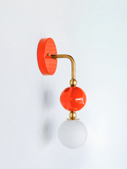A warm, saturated wall sconce for rooms that lead with color and character. This angle of the Ida sconce puts the bold round flame-orange backplate front and center, with a brass arm curving down to a glossy orange sphere and frosted glass globe. Sunny, citrusy, and confident, it's a spirited pick for colorful bathrooms, powder rooms, entryways, and maximalist spaces that want one joyful, standout detail.