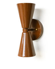 There's something quietly sultry about a lacquered brown fixture, and this Dryades sconce delivers it in a crisp mid-century silhouette. Seen from the side, the two cones taper away from a brass center collar, with the glossy Fudge Brown powder coat catching the light along each ridge. It's a versatile scale for a powder room, an entry, or a pair flanking a bed, and the chocolate tone brings warmth without going dark. Ideal for a home that mixes eras and isn't afraid of a saturated, characterful color.