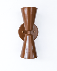 There's something quietly sultry about a lacquered brown fixture, and this Dryades sconce delivers it in a crisp mid-century silhouette. Seen from the side, the two cones taper away from a brass center collar, with the glossy Fudge Brown powder coat catching the light along each ridge. It's a versatile scale for a powder room, an entry, or a pair flanking a bed, and the chocolate tone brings warmth without going dark. Ideal for a home that mixes eras and isn't afraid of a saturated, characterful color.