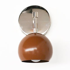 Studio close-up of the Loa wall sconce in fudge brown and polished chrome. A glossy, milk-chocolate brown powder-coated steel dome shade hangs from a round chrome backplate with a sleek swivel arm. Clean, modern lighting for a bathroom vanity, bedside reading nook, hallway, or entryway. Great for mid century modern, Scandinavian, and contemporary interiors that want a warm brown accent with shiny chrome hardware.