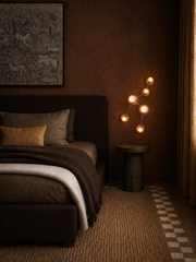 A dark, atmospheric bedroom designed in a deeply layered brown palette, with tonal walls, brown curtains, plush bedding, and a tailored upholstered bed for a cocoon-like, high-end look. The Taurus sconce by Sazerac Stitches glows warmly on the wall, emphasizing its star-inspired silhouette and sculptural arrangement of globe bulbs and round shades. This image is strong for searches related to moody luxury bedroom inspiration, masculine bedroom lighting, warm ambient wall sconces, color-drenched bedroom desi