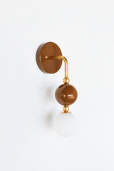 Rich, cozy vanity lighting for a bathroom, powder room, or moody bedroom with a warm point of view. Shown nearly head on, the Ida sconce stacks a glossy chocolate-brown powder-coated sphere over a frosted glass globe, joined by warm brass hardware and a round brown backplate. Deep, caramel-toned, and enveloping, it's a standout for eclectic, English cottage, and colorful traditional interiors that reach for warm color instead of beige.