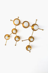 Studio photo of the Gemini One sconce in all brass, designed to echo the stars of the Gemini astrological constellation. The sculptural brass wall light uses mixed round disc sizes, connected brass arms, and white globe bulbs to create a celestial star-map effect. A modern zodiac sconce for astrology-inspired interiors, mid century modern lighting, hallway wall decor, powder rooms, bedrooms, and statement bathroom vanity lighting.