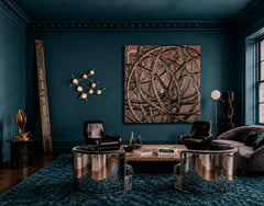 Moody monochromatic teal lounge with a brass Gemini One sconce on the wall, styled like sculptural constellation art in a masculine mid-century modern space. The room mixes deep teal walls, a plush teal rug, black leather chairs, chrome lounge seating, abstract wall art, and dark wood accents for an aeronautical, vintage collector feel. This image works for customers looking for brass wall sconces, zodiac lighting, constellation wall lights, masculine living room lighting, moody interiors, and statement lig
