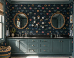 Playful coastal bathroom with dark blue fish and shell wallpaper, deep teal double vanity cabinets, black countertop, two round woven mirrors, striped hand towels, and a chrome Gemini One sconce centered between the mirrors. The constellation-inspired wall light has chrome rods, circular metal details, and white globe bulbs, adding modern zodiac lighting to a nautical family bathroom. This image is ideal for coastal bathroom ideas, kids bathroom lighting, maximalist wallpaper, chrome wall sconces, and state