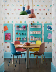 Colorful kids’ craft room with three pendant lights, bright chairs, playful wallpaper, and organized art supplies — creative playroom inspiration.