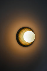 Angled studio view of a glossy plaid ceramic wall sconce in lime green, cream, and pale blue with a matte white globe shade, emphasizing the curved ceramic silhouette and reflective glaze, a colorful statement globe sconce for dopamine decor, eclectic modern interiors, playful wall lighting, and design-forward accent lighting in entryways, bedrooms, and powder rooms.