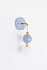 Calm, sophisticated vanity lighting that gives a bathroom, powder room, or bedroom a quiet point of view. Seen in profile, the Ida sconce shows off its curved brass arm reaching from a glossy dove-grey backplate down to a stacked grey sphere and frosted glass globe. The side view highlights the brass ball detailing and how far the fixture projects off the wall. A soft, easy-to-live-with choice paired with warm brass for organic modern, transitional, and colorful traditional interiors.