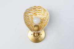 Sculptural shell sconce shown from the side, highlighting the glossy hand-painted cream and gold pattern, fluted powder-coated steel construction, and detailed brass arm and base; statement lighting for eclectic interiors