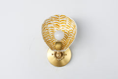 Cream and gold hand-painted Coquille Sconce featuring a fluted powder-coated steel shade with warm ochre strokes, E26 bulb socket, and decorative brass mounting plate; unique coastal Art Deco wall light