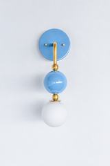 A statement wall sconce for rooms that want color with a soft, romantic feel. This angle of the Ida sconce puts the bold round periwinkle backplate front and center, with a brass arm curving down to a glossy blue sphere and frosted glass globe. Pretty, gentle, and quietly confident, it's a soothing pick for romantic bedrooms, colorful bathrooms, girls' rooms, and grandmillennial spaces that want one soft, standout detail.