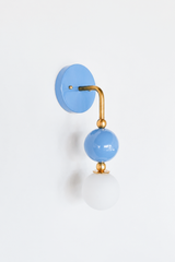 Soft, pretty vanity lighting that gives a bathroom, powder room, or romantic bedroom a gentle point of view. Seen in profile, the Ida sconce shows off its curved brass arm reaching from a glossy periwinkle backplate down to a stacked blue sphere and frosted glass globe. The side view highlights the brass ball detailing and how far the fixture projects off the wall. A romantic, dried-hydrangea-blue choice for Southern traditional, grandmillennial, and colorful traditional interiors.