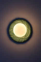 Lit green ceramic globe sconce, jade glazed leafy relief backplate with warm frosted globe, moody ambient light for hallway, bedroom, or bath