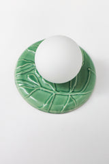 Jade green ceramic wall sconce detail, glossy leaf relief on round backplate with frosted globe, chinoiserie-inspired botanical accent lighting
