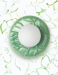 Close-up of the Jade Green Lierre ceramic wall sconce by Sazerac Stitches, featuring a glossy jade green, leaf-relief backplate with sculpted botanical texture and a white frosted globe shade, styled against airy leafy line-art wallpaper in soft greens on a white background. Fresh garden-inspired decor with a modern organic feel, blending vintage botanical wallpaper, nature motif lighting, and colorful ceramic craftsmanship for a statement powder room, bathroom vanity, hallway, or cozy cottagecore interior.