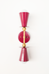 This vertical bath bar sconce is built to flank a bathroom mirror in pairs, with two Black Cherry cone shades and brass ball hardware giving it a mid-century, Art Deco-adjacent shape. The deep wine tone reads more moody and sophisticated than the brand's brighter colorways, making it a good fit for a powder room, a home bar, or a hallway that wants some drama. Symmetrical shape, rich color, made to actually get noticed instead of disappearing into the wall.