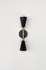 Black Janus Sconce with brass center column and accents, a bold geometric two light wall sconce with tapered cone shades and minimalist disc plates, photographed straight on with globe bulbs, a modern brutalist inspired wall light that installs vertical or horizontal, perfect for bathroom vanity lighting, mirror sconces, bedroom reading lights, entryway lighting, and designer modern home decor