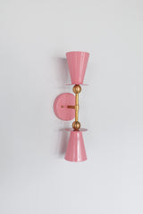 Blush pink Janus Sconce, a bold architectural two light wall sconce with stacked tapered cone shades, flat disc details, and warm brass hardware, shown mounted vertically with globe bulbs, a modern sculptural brutalist meets mid century modern wall light for bathroom vanity lighting, hallway sconces, bedroom bedside lighting, and statement lighting in design forward interiors