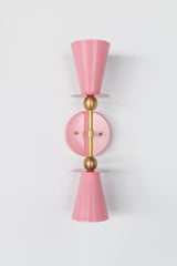 Blush pink Janus Sconce, a bold architectural two light wall sconce with stacked tapered cone shades, flat disc details, and warm brass hardware, shown mounted vertically with globe bulbs, a modern sculptural brutalist meets mid century modern wall light for bathroom vanity lighting, hallway sconces, bedroom bedside lighting, and statement lighting in design forward interiors