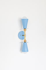 This sconce is built around two identical cone shades in celestial blue, mounted opposite each other on a vertical brass stem. Each cone sits on a flat brass disc and rests against a brass ball joint, with an exposed bulb glowing at the open end. The cone shape nods to Art Deco lighting, while the round bulbs and brass ball hardware keep it feeling mid-century. A round backplate holds the whole fixture flat against the wall.