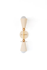 Full studio view of the Janus Sconce, a geometric two-light fixture with cream cone shades, brass accents, and a sculptural stacked form. It has a playful, art-object quality that brings personality to a room while still feeling polished and intentional. This is a strong fit for colorful lighting lovers, maximalists, quirky interior designers, dopamine decor, kids rooms, boutique bathrooms, and anyone searching for a modern brass wall sconce with custom powder-coated color options.