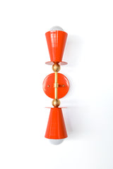 Flame orange Janus sconce installed vertically with brass stem and two cone shades, modern double bulb wall light for bathroom sconces, entryway, hallway, bedroom, or stairwell, colorful statement lighting for maximalist design and playful contemporary decor.