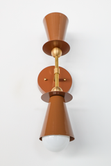 A fudge-brown double cone hangs like an hourglass from the ceiling, one shade pointing up, one down, separated by a gleaming brass sphere. This is architectural jewelry—a fixture that reads as sculpture first, functional light second. The warm, earthy brown plays against polished brass in a composition that feels both brutalist and refined. Perfect for an entryway, stairwell, or any space that deserves a statement piece with serious design presence. The opposing cones create a visual anchor that anchors a r