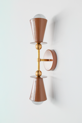 From the side, this fudge-brown sconce reveals its clean, architectural bones: a tapered cone that catches light from above, a brass rod that extends with intention, and a simple sphere finial that grounds the composition. The profile reads like restrained modernism—no excess, no ornamentation, just warm color paired with polished brass and thoughtful proportion. This is the kind of sconce that works alone or in pairs, in a master bedroom or a kid's room, beside a mirror or flanking a doorway. It's a workho