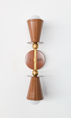 Fudge brown cones point in opposite directions from a brass-accented wall mount—a sconce that reads like wall-mounted sculpture. The Janus form creates visual rhythm and architectural interest, the warm brown paired with brushed brass delivering both warmth and refinement. Mount this in a hallway to draw light upward and downward simultaneously, or frame a doorway with a pair for balanced, symmetrical drama. The opposing geometry makes it feel collected and intentional—like you found a rare modernist artifa