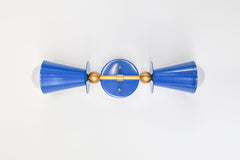 Turned on its side, the Janus Sconce shows off just how deliberate its symmetry is: two cobalt cone shades balanced by brass ball joints on either side of a round backplate, like a piece of jewelry more than a light fixture. It's a good angle for appreciating the hardware and proportions before picturing it mounted and lit on an actual wall.
