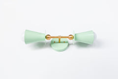 Angled view of the Janus Sconce in glossy yellow with brass backplate and center rod, showing stacked geometric double cone shades with soft globe bulbs, a sculptural modern wall sconce with mid century modern and brutalist design influence, ideal as a bathroom wall sconce, mirror side lighting, hallway statement light, bedroom wall light, or designer accent fixture in color forward interiors.