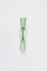 Front product view of the Janus Sconce in yellow and brass on a clean background, a symmetrical two light wall fixture with tapered cone shades, circular discs, and globe bulbs, architectural modern lighting with mid century modern and brutalist style, suitable for bathroom vanity wall lighting, entryway lighting, corridor lighting, bedroom reading wall light, and bold contemporary or maximalist home decor.