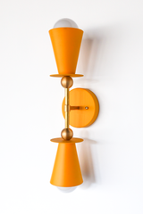 This mustard vanity sconce brings a warm, golden pop of color to a kitchen, entryway, or breakfast nook, and works just as well flanking a bathroom mirror in pairs. The double cone shape and brass ball hardware keep the silhouette clean and symmetrical, so the color gets to do the talking. A strong choice for anyone building an English cottage or traditional palette with real warmth.
