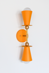 This vertical bath bar sconce is built to flank a bathroom mirror in pairs, with two mustard cone shades and brass ball hardware giving it a mid-century, Art Deco-adjacent shape. The warm golden tone works well in a powder room, a breakfast nook, an entryway, or anywhere leaning into an English cottage or traditional color palette. Symmetrical shape, cheerful color, made to actually get noticed instead of disappearing into the wall.