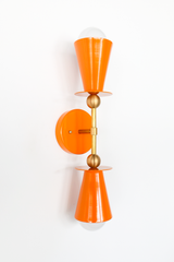 This Orange Peel vanity sconce brings a citrusy jolt of color wherever it lands, whether that's flanking a bathroom mirror, adding warmth to a breakfast nook, or lighting up a hallway. The double cone shape and brass ball hardware keep the silhouette clean and symmetrical, so the color does the talking. A good pick for anyone who wants their lighting to read as a real design choice, not an afterthought.
