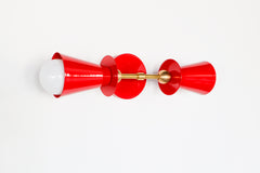 A closer look at how the bulb sits inside the cone shade on this red and brass vanity sconce. Installed, this fixture mounts vertically in pairs on either side of a bathroom mirror, giving a powder room or hallway a warm, symmetrical light source with real personality. The brass ball hardware and glossy red finish hold up just as well up close as they do from across the room.
