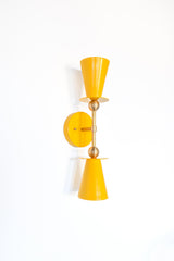 Yellow & Brass Janus Sconce, a bold architectural two light wall sconce with stacked tapered cone shades, flat disc details, and warm brass hardware, shown mounted vertically with globe bulbs, a modern sculptural brutalist meets mid century modern wall light for bathroom vanity lighting, hallway sconces, bedroom bedside lighting, and statement lighting in design forward interiors
