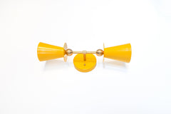 Yellow & Brass Janus Sconce, a bold architectural two light wall sconce with stacked tapered cone shades, flat disc details, and warm brass hardware, shown mounted vertically with globe bulbs, a modern sculptural brutalist meets mid century modern wall light for bathroom vanity lighting, hallway sconces, bedroom bedside lighting, and statement lighting in design forward interiors