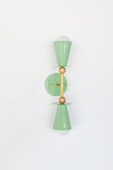 Front view of the Janus Sconce in Vista Green and brass, a two light wall sconce with stacked cone shades, disc details, and globe bulbs in a bold architectural silhouette, ideal as a mid century modern bathroom vanity light, modern hallway wall light, bedroom wall sconce, or sculptural statement lighting for colorful, design forward interiors.