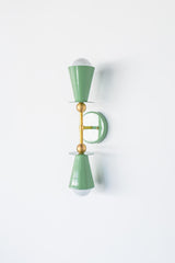 Side perspective of the Janus two light wall sconce in Vista Green and brass, featuring a balanced dual cone design inspired by brutalist and mid century modern lighting, suitable for vertical or horizontal mounting over a vanity, beside a bed, or in an entry hall, perfect for color drenched interiors, modern eclectic spaces, and designer residential projects.