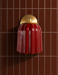 Deep brown subway tile gets its jewel-tone moment from the Marcella Sconce in Jasper Red, its fluted bell shade and brass ball finial standing out against a monochrome wall. This is the kind of pairing that answers what to do with a moody tile bathroom: skip the neutral fixture and let the color do the talking. Ideal inspiration for anyone searching brown bathroom tile ideas or colorful sconces for dark tile.