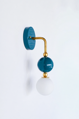 Deep, colorful vanity lighting that gives a bathroom or powder room a moody point of view. Seen in profile, the Ida sconce shows off its curved brass arm reaching from a glossy teal backplate down to a stacked teal sphere and frosted glass globe. The side view highlights the brass ball detailing and how far the fixture projects off the wall. A saturated, sophisticated choice for coastal traditional, grandmillennial, and English cottage interiors.