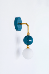 A deep teal wall sconce for a bathroom, powder room, or bedroom that leads with rich, saturated color. The Ida sconce pairs a glossy teal powder-coated sphere with a frosted glass globe, joined by warm brass hardware and a round teal backplate. Peacock-deep and confidently colorful, it's a standout for coastal traditional, grandmillennial, Chinoiserie, and colorful traditional homes that skip the safe answer.