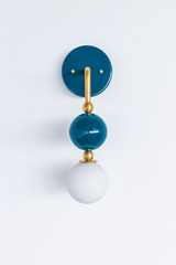 Rich, saturated vanity lighting for a bathroom, powder room, or moody bedroom with a point of view. Shown straight on, the Ida sconce stacks a glossy deep-teal powder-coated sphere over a frosted glass globe, joined by warm brass hardware and a round teal backplate. The head-on view shows how the spheres line up into a tidy vertical drop. Peacock-deep and jewel-toned, it's a standout for colorful traditional, coastal traditional, and grandmillennial interiors.